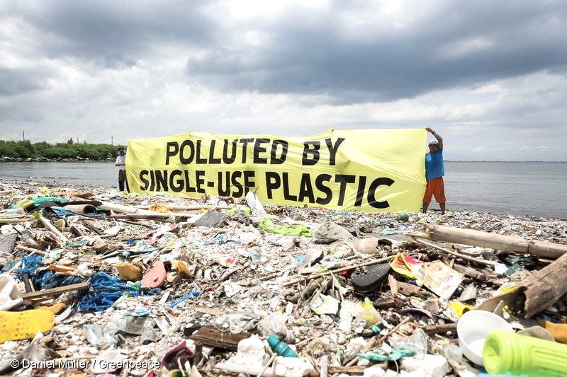 Aktivis Greenpeace membentangkan spanduk bertuliskan “POLLUTED BY SINGLE-USE PLASTIC” di tengah timbunan sampah plastik sekali pakai yang mencemari pesisir Bali. Foto: Daniel Muller/Greenpeace.