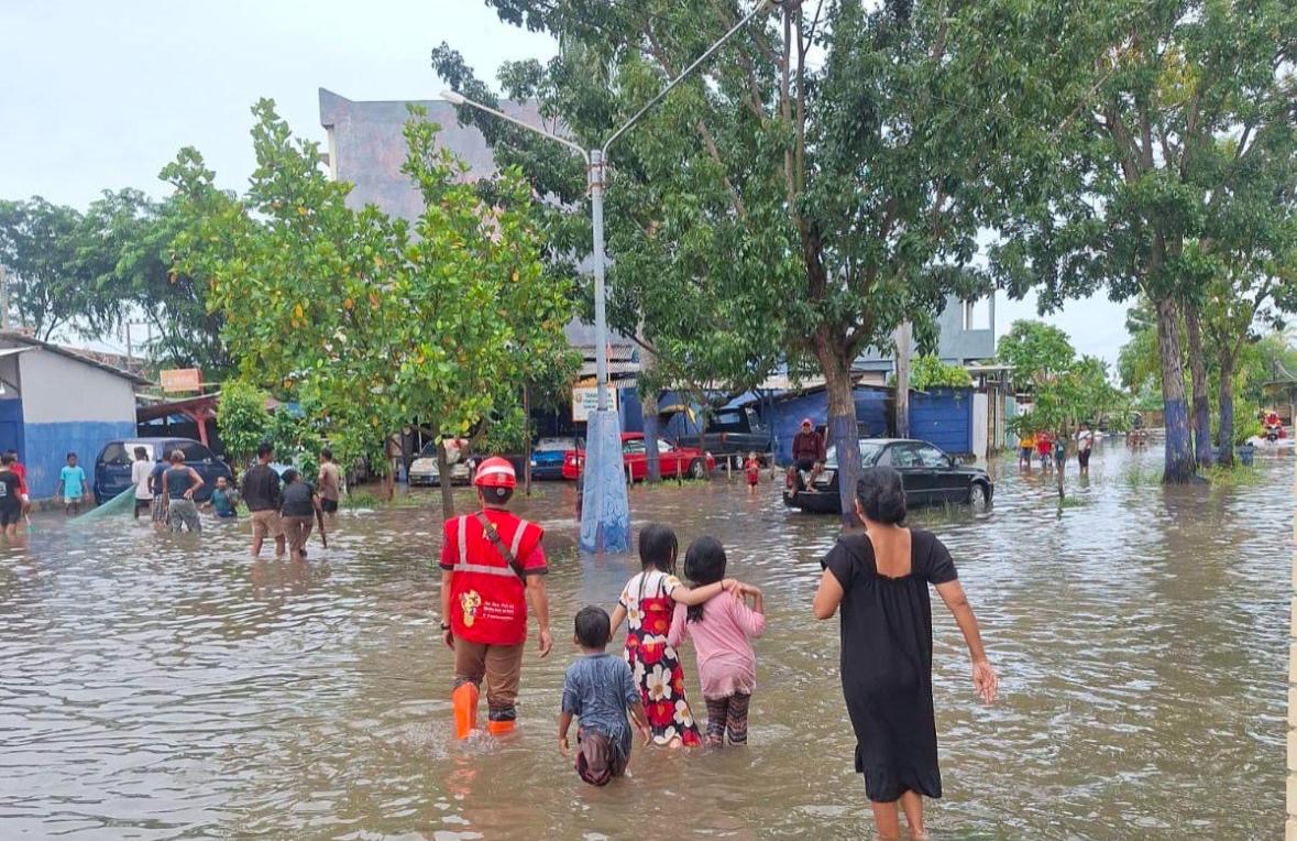 Sejumlah warga bersama petugas terlihat berjalan menerobos banjir yang menggenangi permukiman di sebuah kawasan perkotaan. Foto: Dok. PLN
