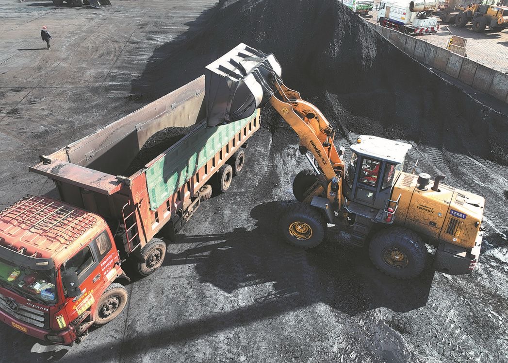 Pekerja mengoperasikan alat berat untuk memuat batu bara ke dalam truk di pelabuhan penambangan China. Foto: China Daily/Wang Chun.