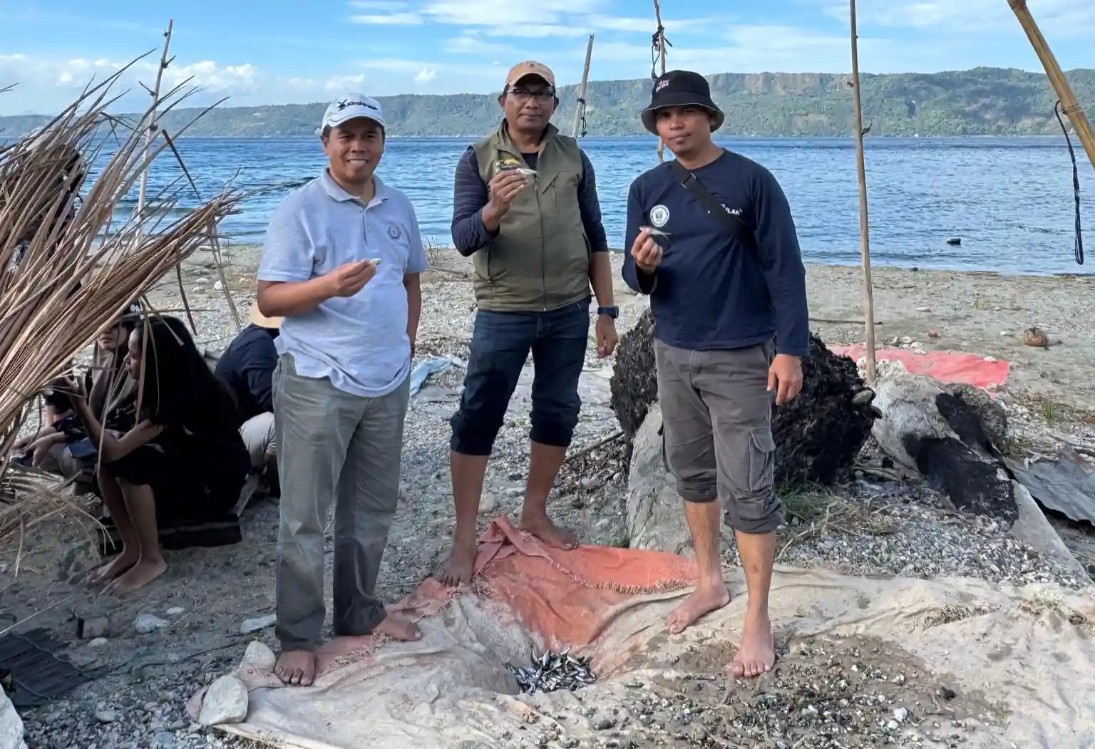 Kepala PKSPL IPB, Prof Yonvitner (kiri), berdiri di tepi Danau Singkarak memegang ikan bilih, spesies endemik yang kini terancam punah. Di depannya, terlihat hasil tangkapan yang belum dewasa dan menjadi simbol krisis ekologis yang membayangi danau terbesar kedua di pulau Sumatera itu. Foto: Dok. PKSPL IPB.