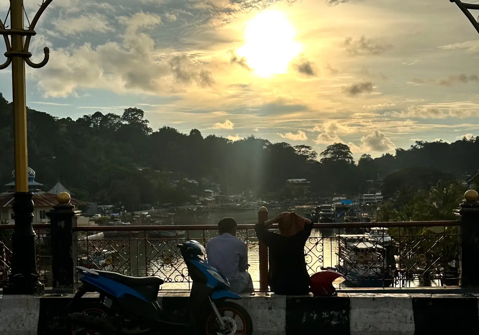 Dua sejoli menikmati senja di Jembatan Siti Nurbaya, Padang, Sumatra Barat. Di balik langit keemasan yang tenang, tren pemanasan global terus menguat, sejalan dengan data terbaru yang menunjukkan suhu Bumi kian mendekati, bahkan melampaui, ambang 1,5 derajat Celsius. Foto: KabarBursa/Moh. Alpin Pulungan