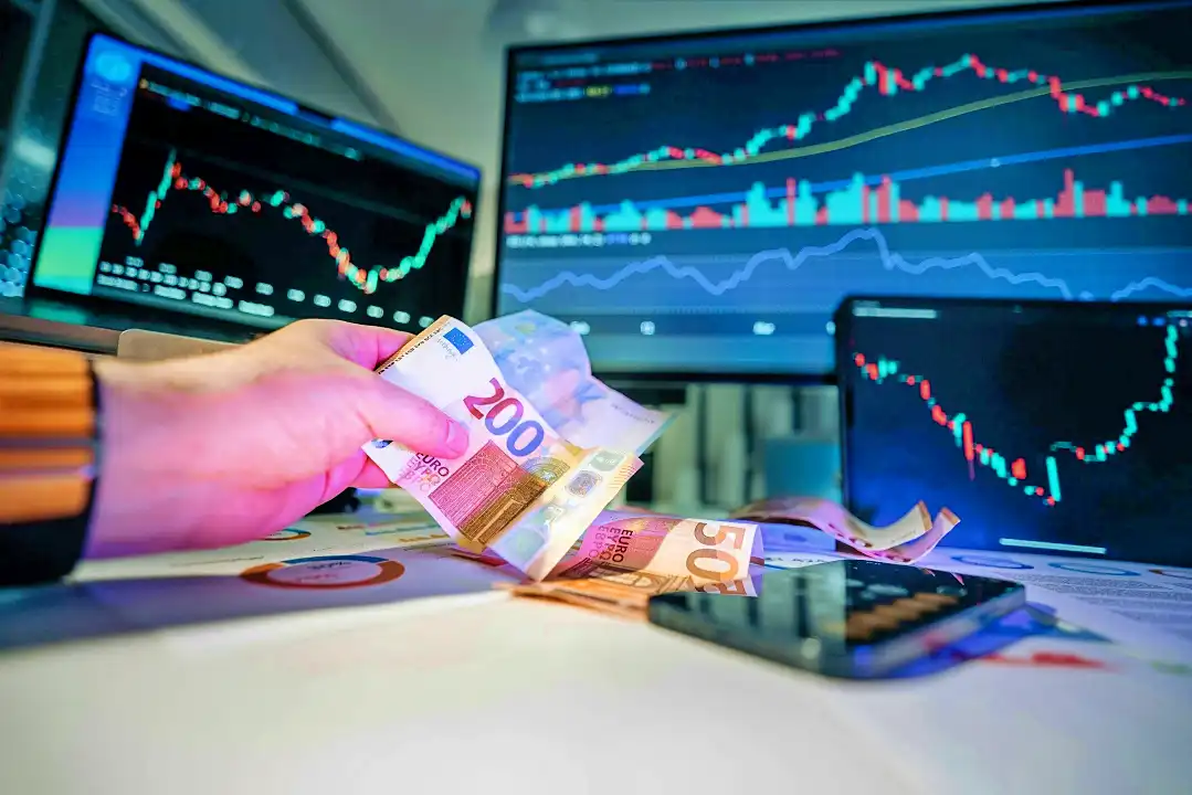 Ilustrasi: Mata uang Euro dengan latar belakang layar monitor yang menampilkan candlestick. (Foto: Pexels/Jakub Zerdzicki)